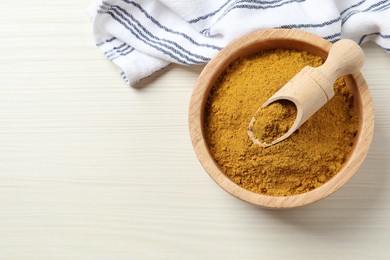 Dry curry powder in bowl and scoop on light wooden table, top view. Space for text