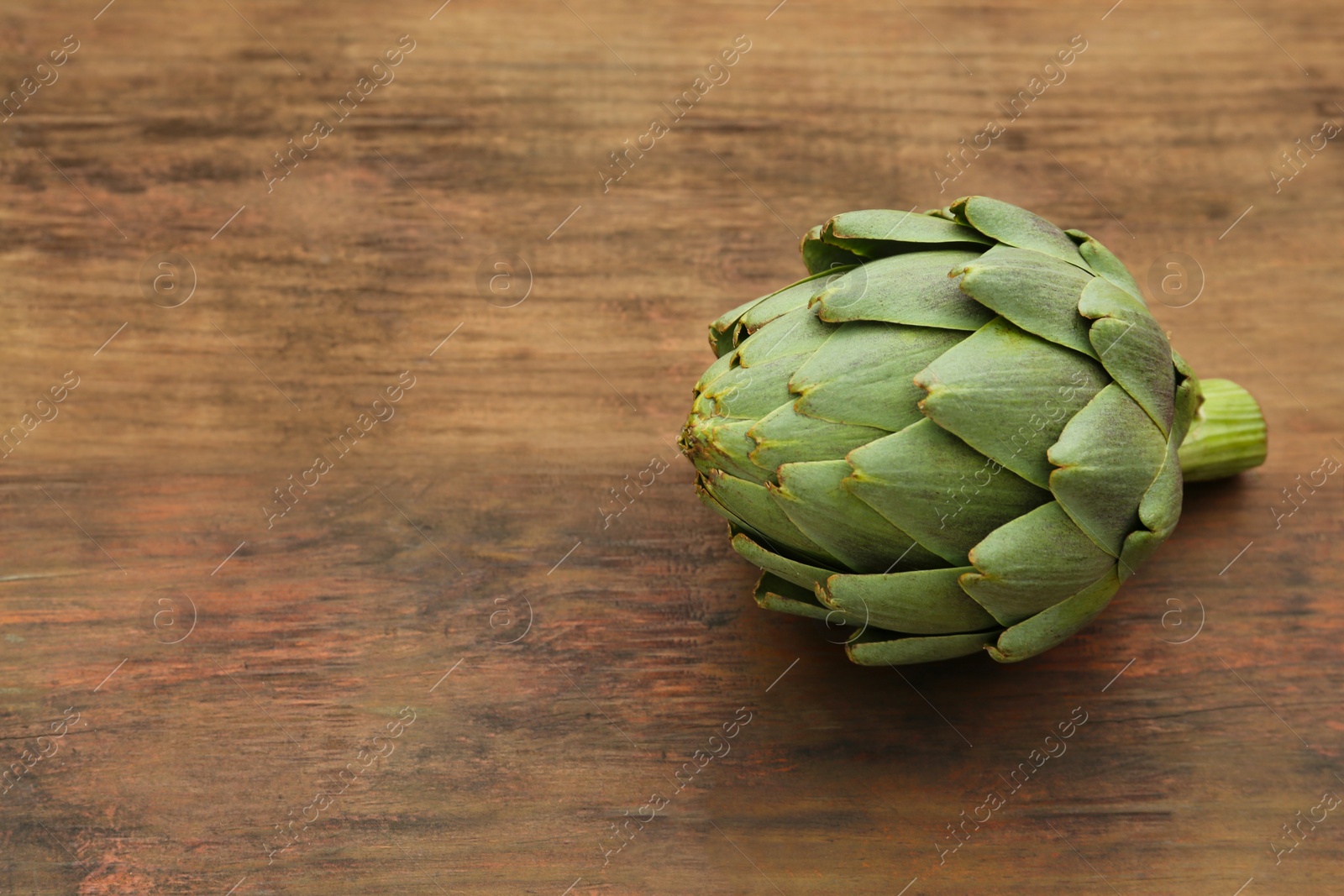 Photo of Fresh raw artichoke on wooden table. Space for text