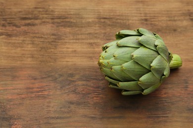 Photo of Fresh raw artichoke on wooden table. Space for text