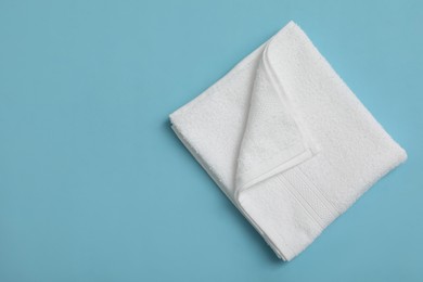 Photo of Folded white beach towel on light blue background, top view. Space for text