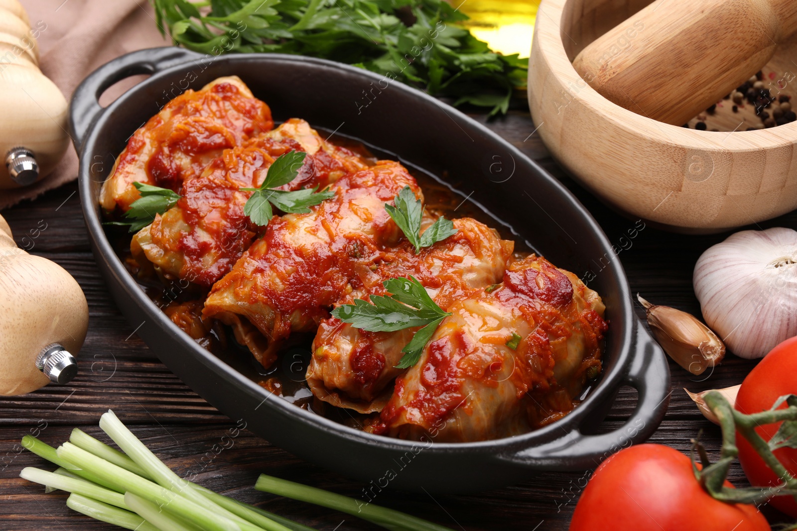 Photo of Delicious stuffed cabbage rolls cooked with tomato sauce and ingredients on wooden table, closeup
