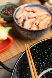 Photo of Black wok, chopsticks and bamboo mat with products on table, closeup