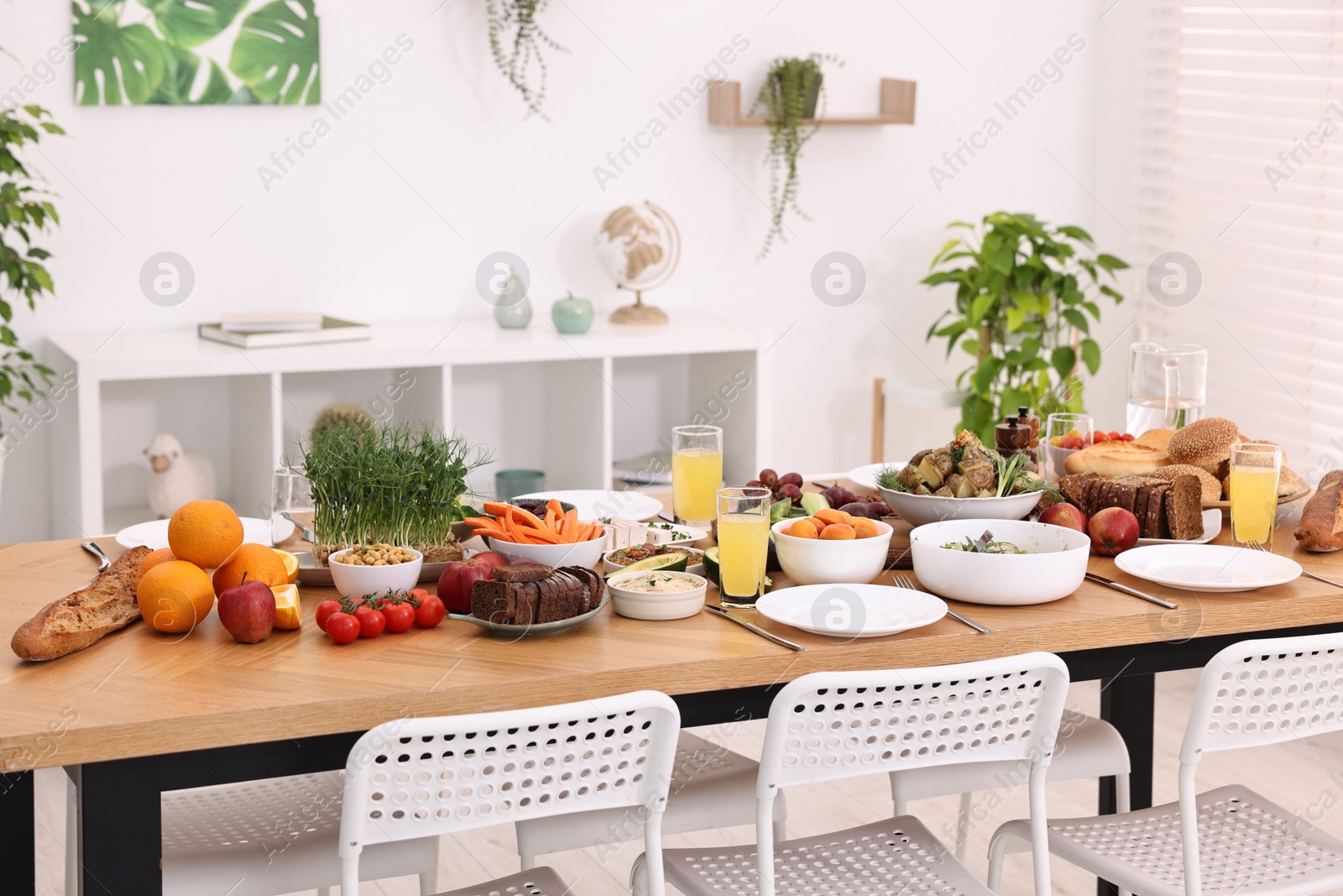 Photo of Healthy vegetarian food, glasses of juice, cutlery and plates on wooden table indoors