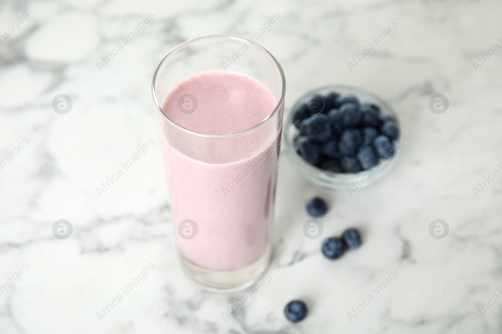 Photo of Tasty milk shake and blueberries on white marble table