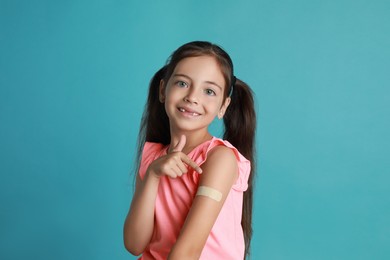 Photo of Vaccinated little girl showing medical plaster on her arm against light blue background
