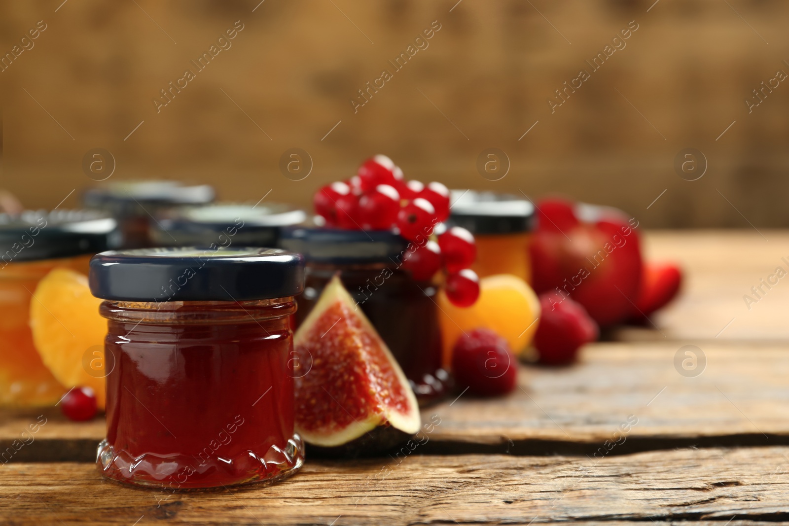 Photo of Jars of different jams and fresh ingredients on wooden table, space for text