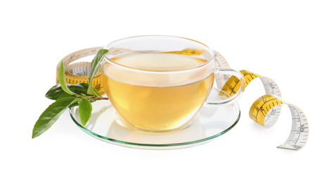 Glass cup of diet herbal tea, green leaves and measuring tape on white background