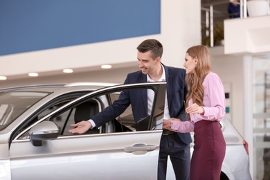 Photo of Young salesman working with client in car dealership