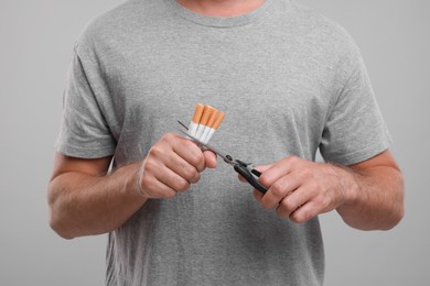Photo of Stop smoking concept. Man cutting cigarettes on grey background, closeup
