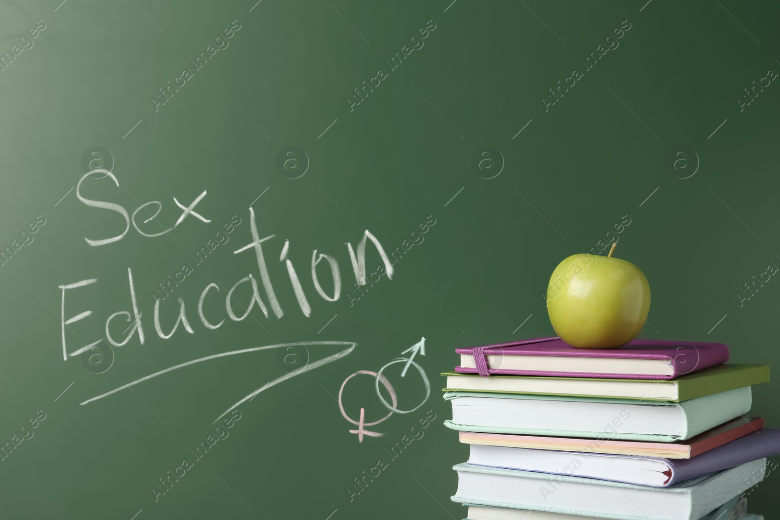 Photo of Books and apple near chalkboard with phrase "Sex education"