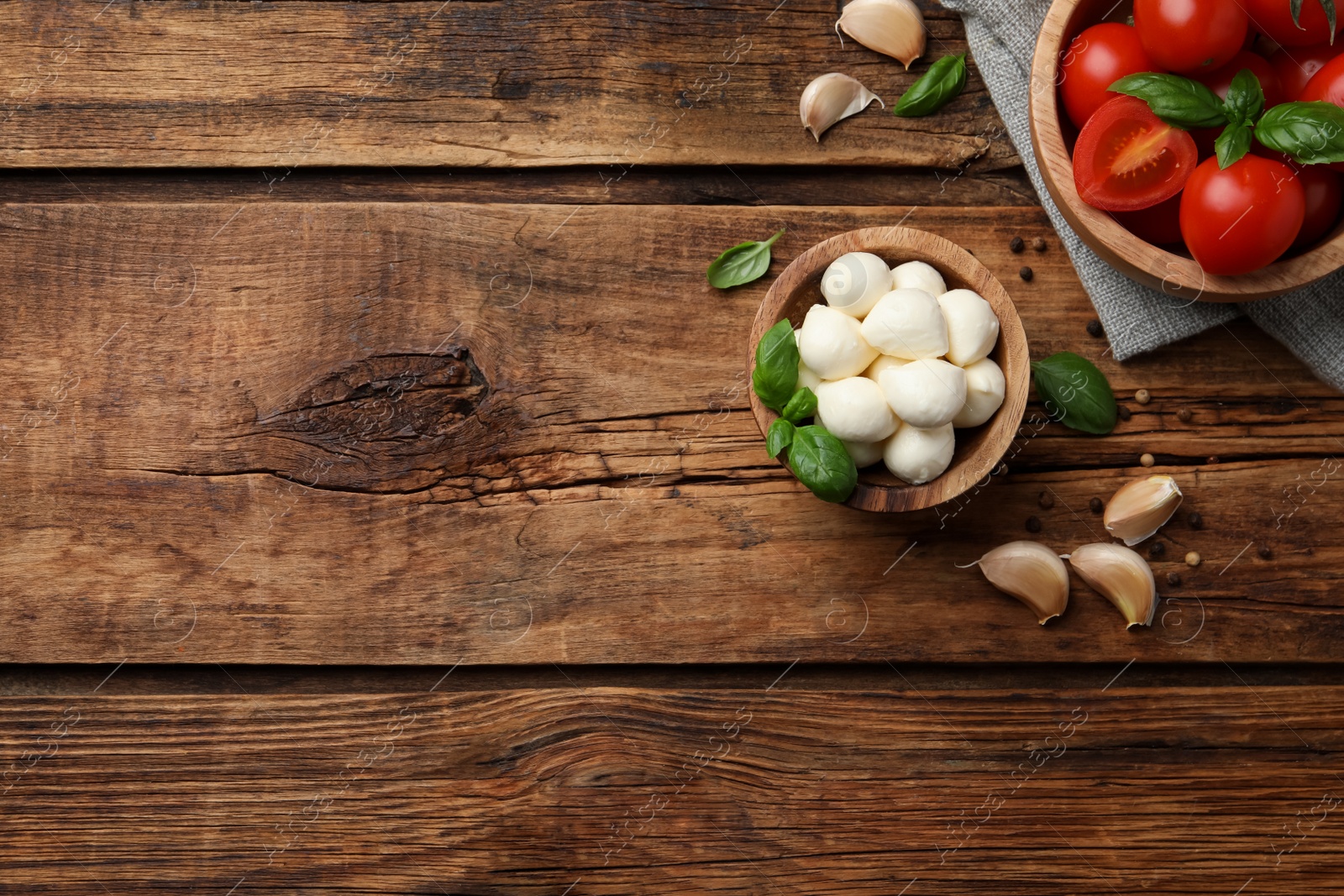 Photo of Delicious mozzarella balls in bowl, tomatoes and basil leaves on wooden table, flat lay. Space for text