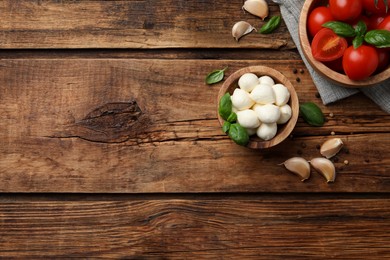 Delicious mozzarella balls in bowl, tomatoes and basil leaves on wooden table, flat lay. Space for text