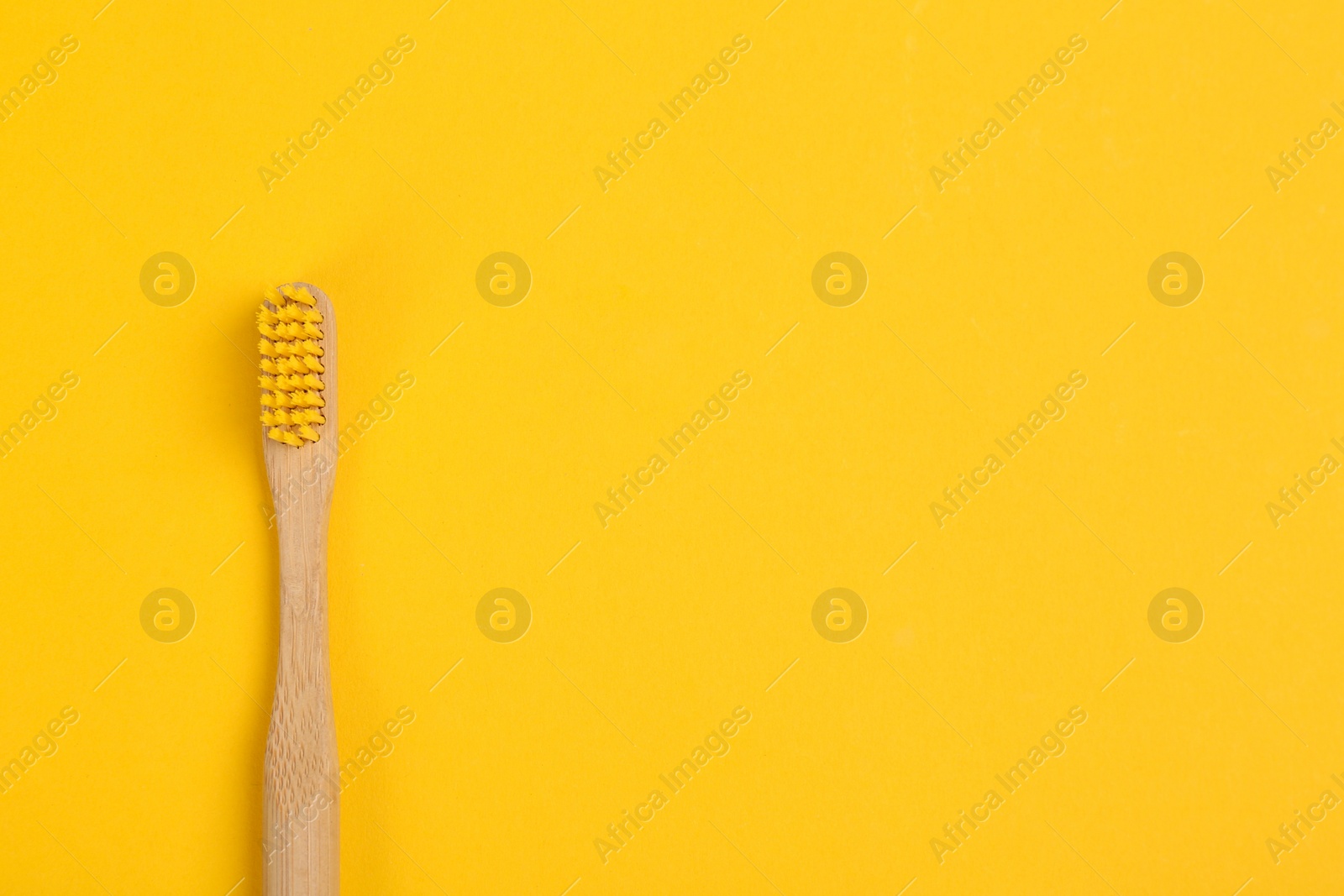 Photo of Toothbrush made of bamboo on yellow background, top view. Space for text