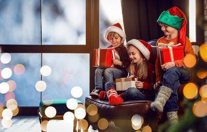 Photo of Little children with Christmas gifts near window indoors. Presents from Santa Claus