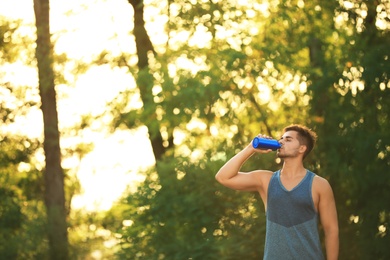 Photo of Young man drinking water from sport bottle after training in park