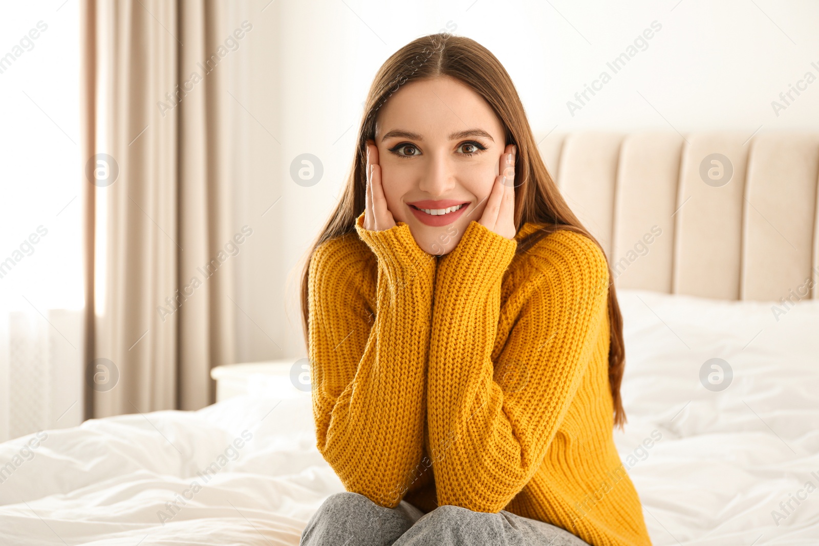 Photo of Young woman wearing warm sweater on bed at home. Winter season