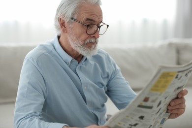 Portrait of grandpa with stylish glasses reading newspaper on sofa indoors