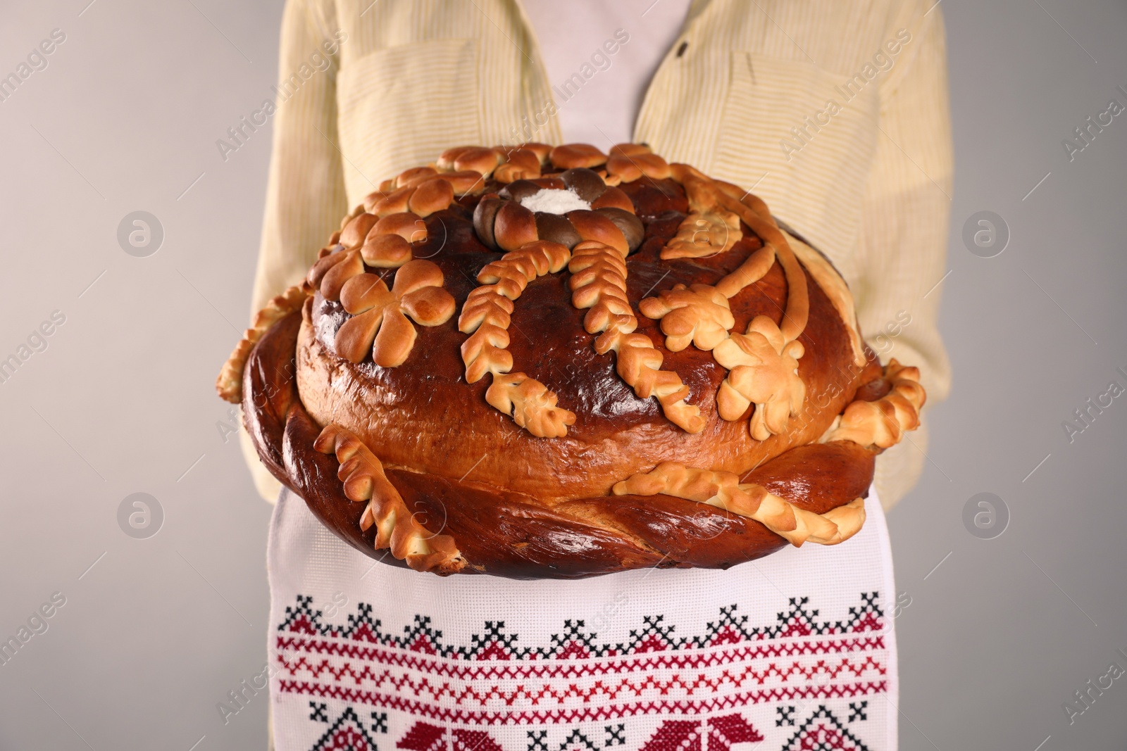 Photo of Woman with korovai on grey background, closeup. Ukrainian bread and salt welcoming tradition