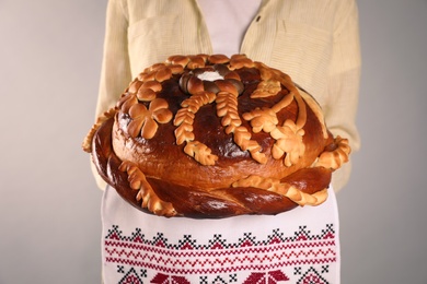 Photo of Woman with korovai on grey background, closeup. Ukrainian bread and salt welcoming tradition