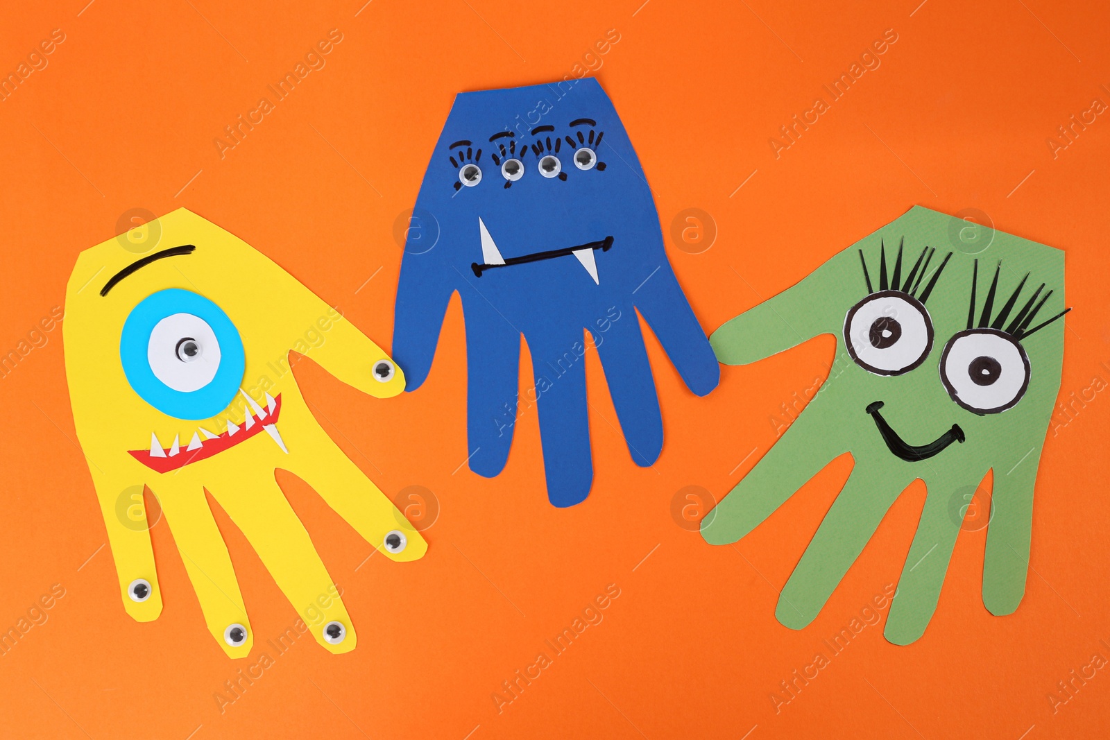 Photo of Funny hand shaped monsters on orange background, flat lay. Halloween decoration