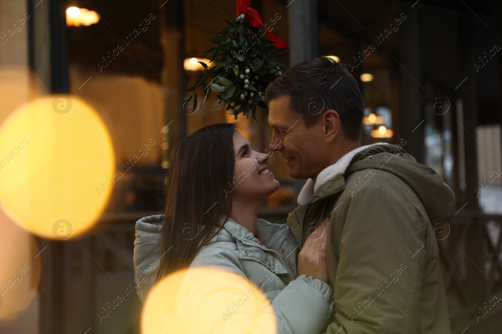 Photo of Happy couple standing under mistletoe bunch outdoors, bokeh effect