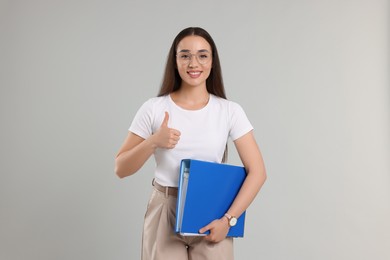 Photo of Happy woman with folder showing thumbs up on light gray background
