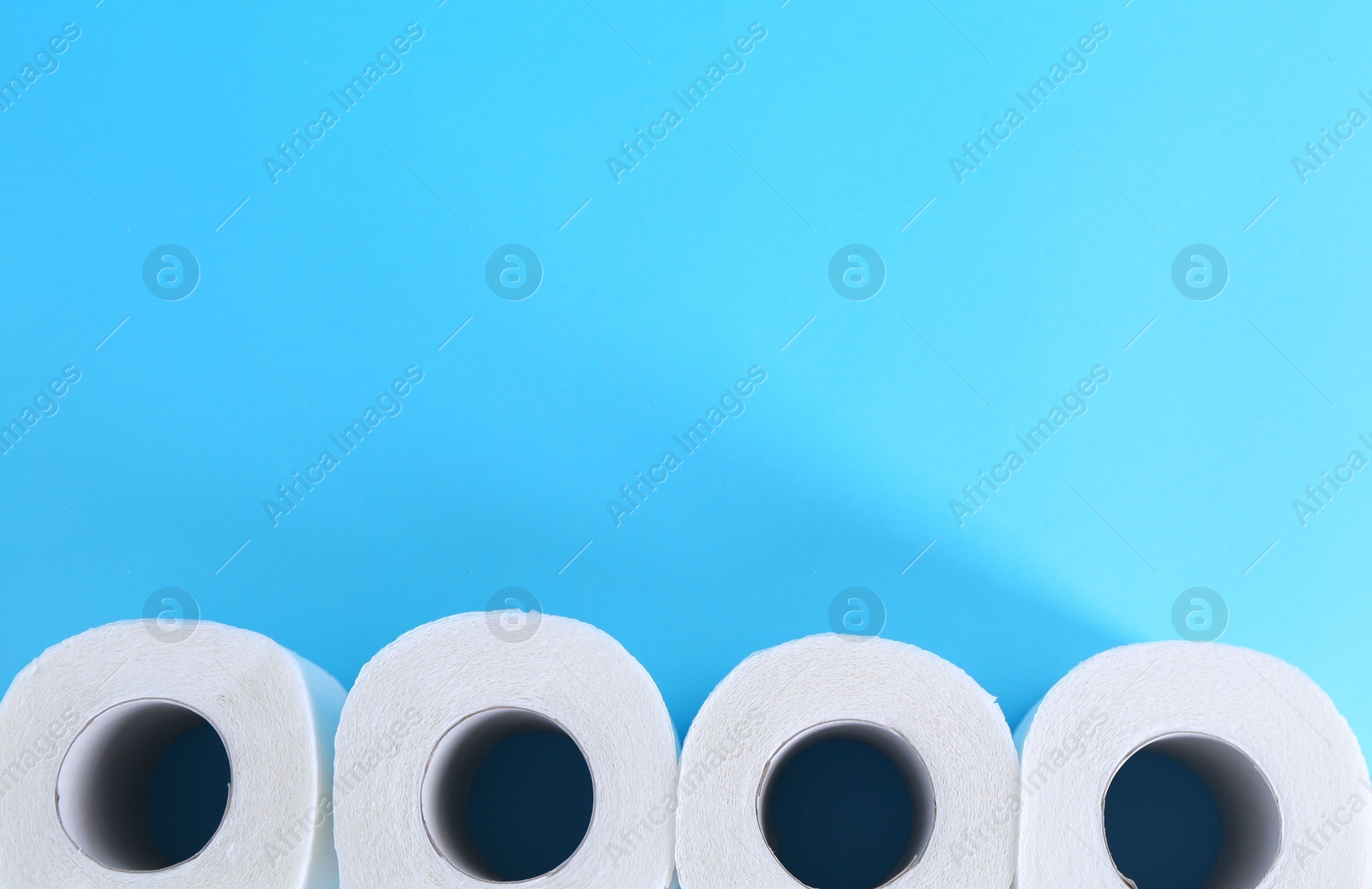 Photo of Soft toilet paper rolls on light blue background, flat lay. Space for text