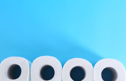 Photo of Soft toilet paper rolls on light blue background, flat lay. Space for text