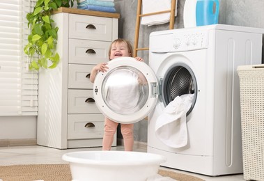 Photo of Happy girl near washing machine with baby clothes in bathroom