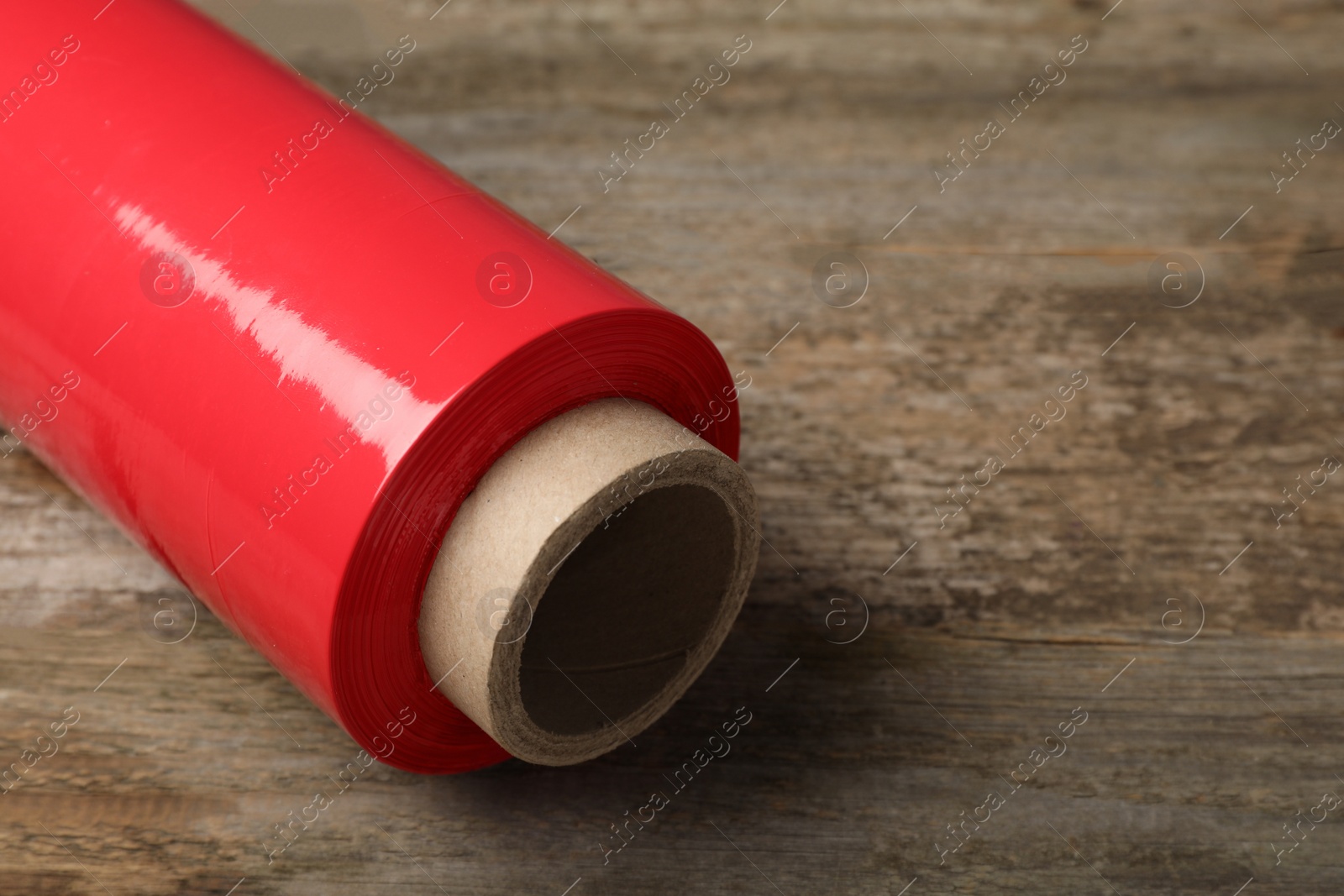Photo of Roll of red plastic stretch wrap on wooden background, closeup. Space for text