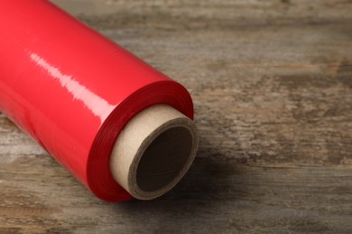 Photo of Roll of red plastic stretch wrap on wooden background, closeup. Space for text