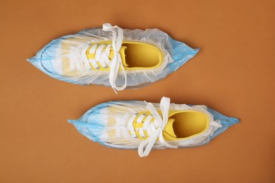 Photo of Sneakers in shoe covers on brown background, top view