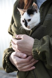 Photo of Soldier in uniform warming little stray cat on blurred background, closeup