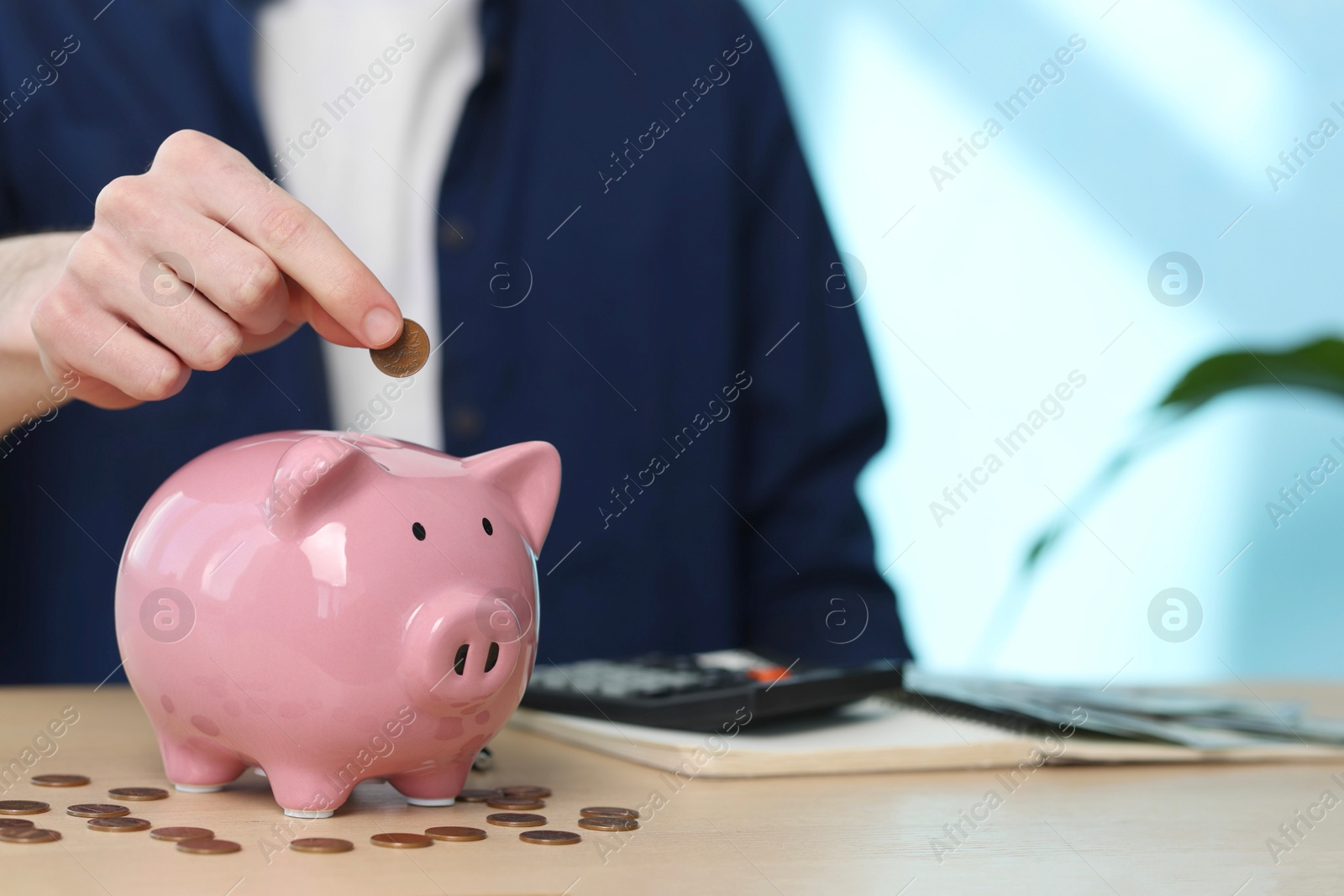 Photo of Financial savings. Man putting coin into piggy bank at wooden table, closeup