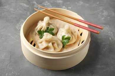 Photo of Bamboo steamer with tasty baozi dumplings and chopsticks on grey background