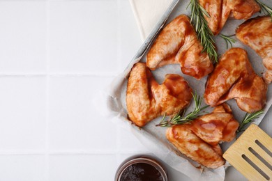 Photo of Raw chicken wings, rosemary and marinade on light tiled table, top view. Space for text