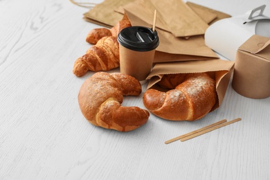 Paper bags with pastry and takeaway food on light table. Space for text