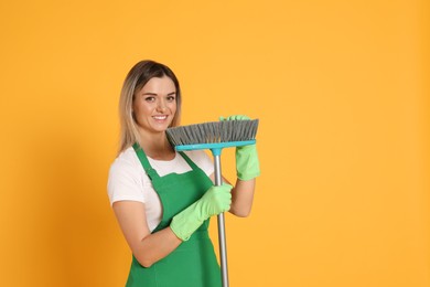 Young woman with broom on orange background, space for text