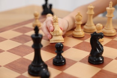 Photo of Little child playing chess, closeup of hand