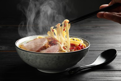 Image of Woman eating hot ramen with chopsticks at black wooden table, closeup. Noodle soup