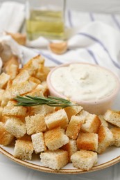 Photo of Delicious crispy croutons with rosemary and sauce on plate, closeup