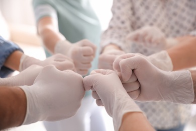 Photo of People in white medical gloves joining fists on light background, closeup