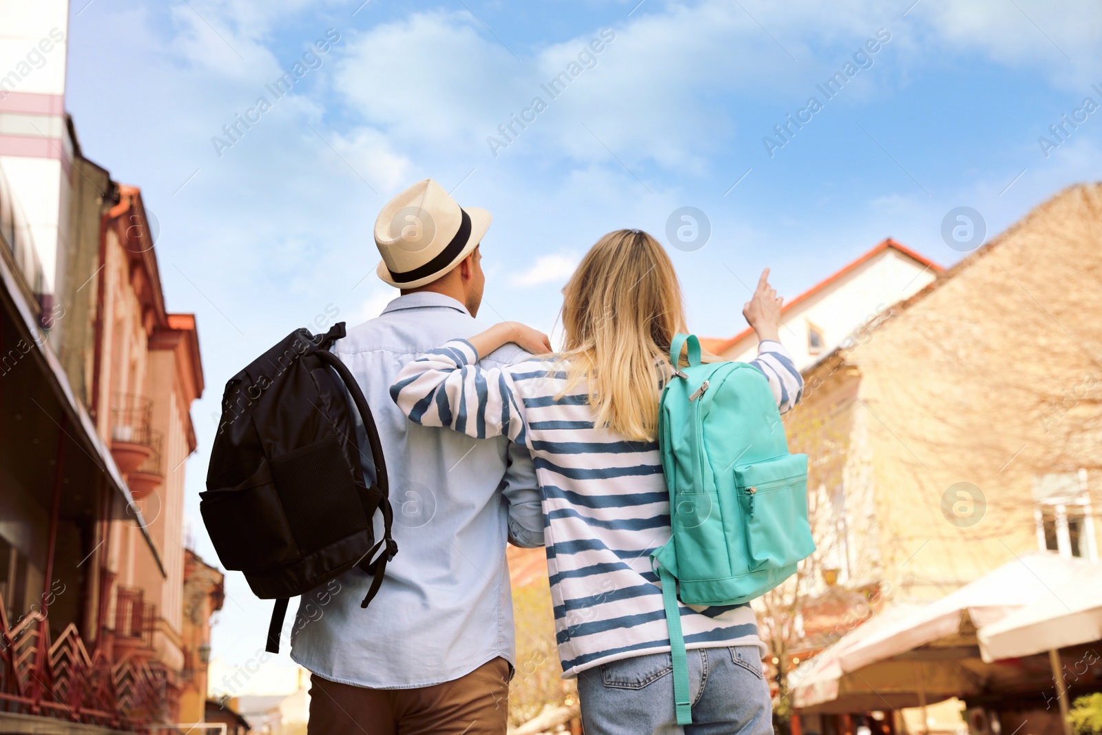 Photo of Couple of tourists with backpacks on city street, back view