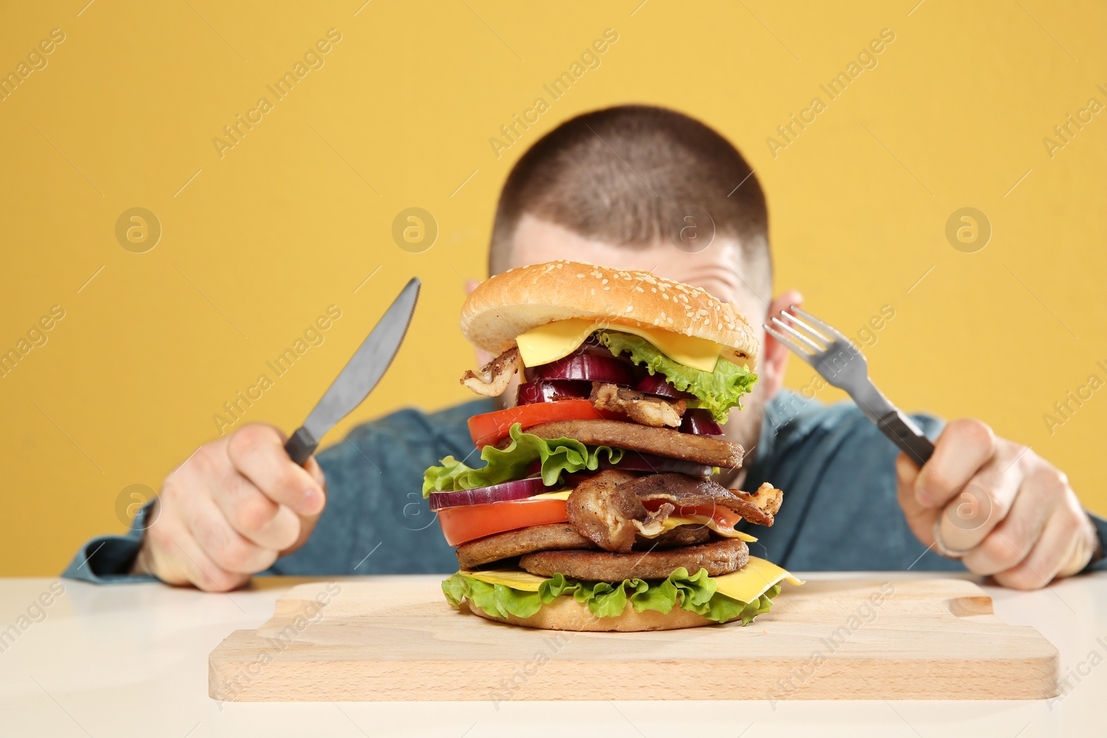 Photo of Young man with cutlery and tasty huge burger at table