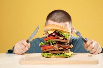Young man with cutlery and tasty huge burger at table