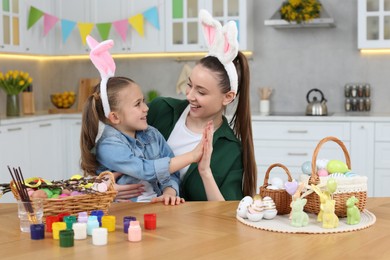 Photo of Happy mother and daughter with Easter eggs at table in kitchen