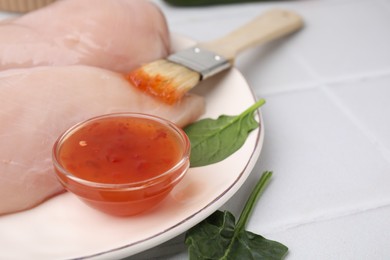 Photo of Marinade, basting brush and raw chicken fillets on white table, closeup. Space for text