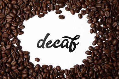 Photo of Word Decaf and coffee beans on white background, top view