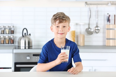 Photo of Adorable little boy with glass of milk in kitchen