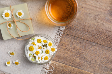 Photo of Flat lay composition with chamomile flowers and cosmetic products on wooden table, space for text